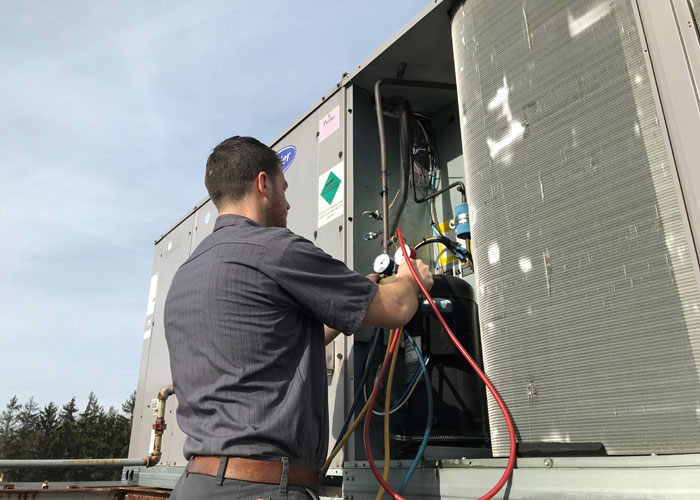 A man is holding two hoses while standing next to an air conditioner.